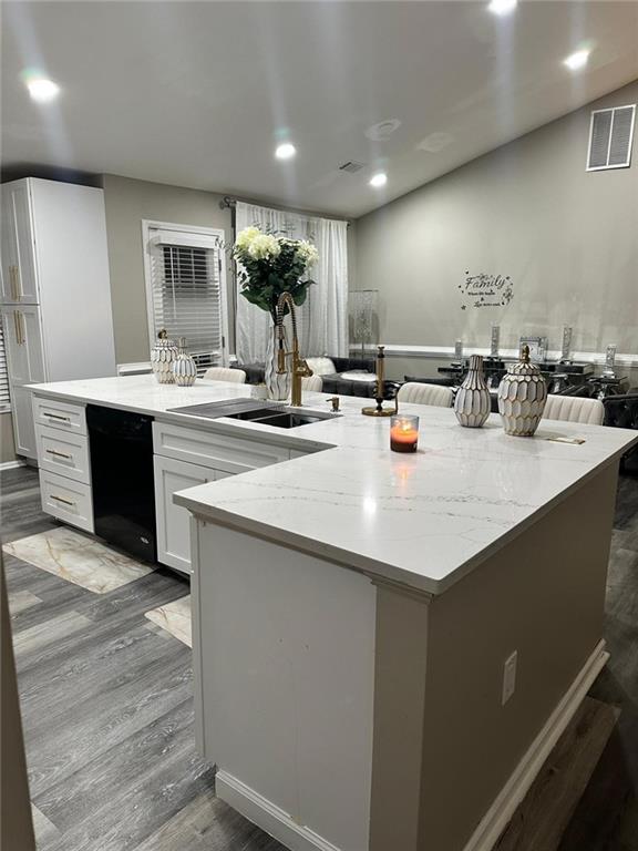 kitchen featuring a sink, black dishwasher, wood finished floors, white cabinetry, and light stone countertops