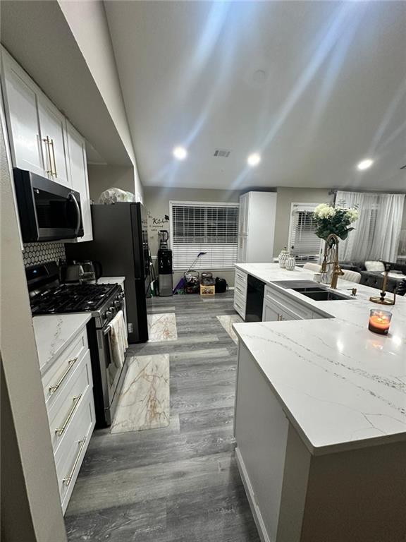 kitchen with visible vents, black appliances, a sink, light stone counters, and tasteful backsplash