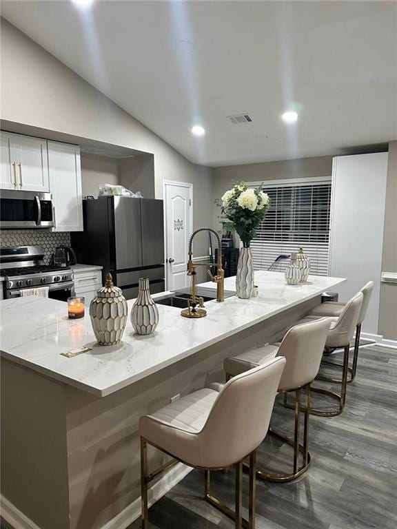 kitchen with visible vents, a breakfast bar, stainless steel appliances, white cabinets, and lofted ceiling