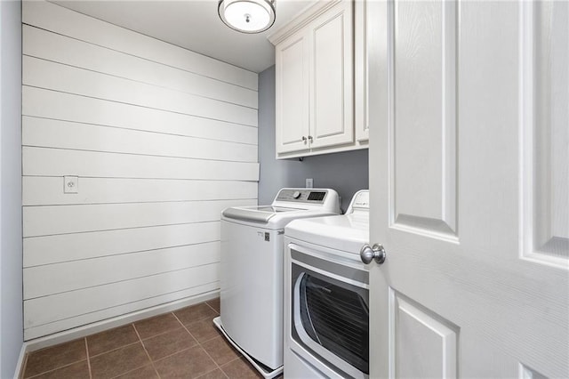 laundry room with wood walls, washer and clothes dryer, cabinets, and dark tile patterned flooring