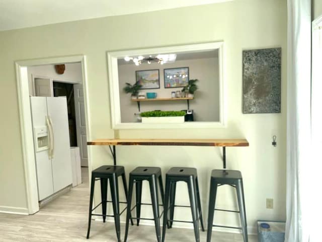 bar featuring light hardwood / wood-style flooring, a chandelier, and white refrigerator with ice dispenser