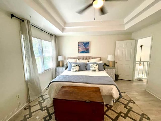 bedroom featuring ceiling fan, a raised ceiling, and light hardwood / wood-style floors