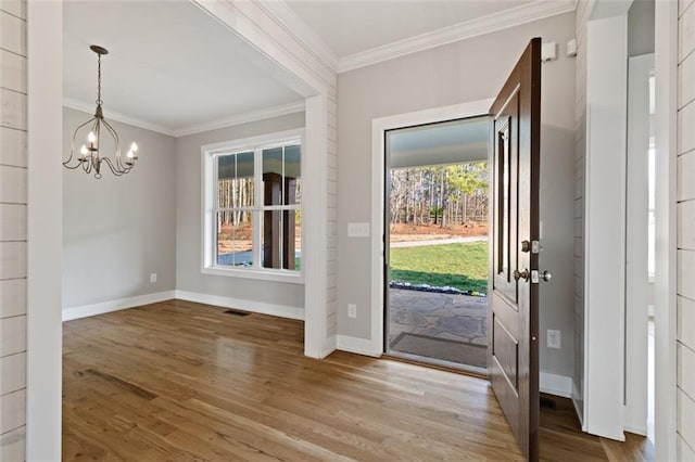 foyer entrance with wood finished floors, visible vents, baseboards, ornamental molding, and a notable chandelier