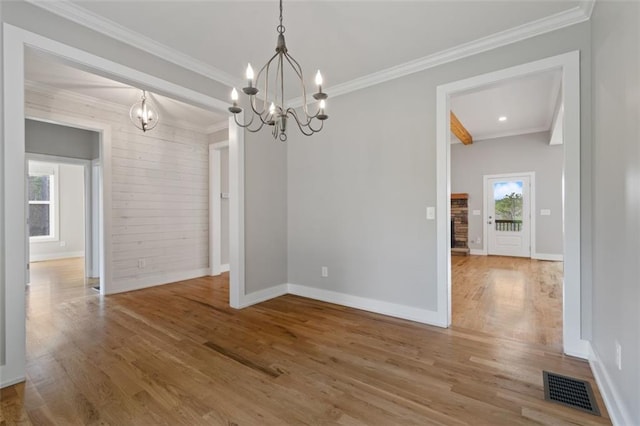 unfurnished dining area featuring visible vents, wood finished floors, a chandelier, and ornamental molding