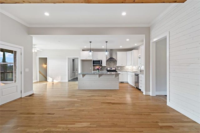 kitchen featuring light wood-type flooring, appliances with stainless steel finishes, crown molding, and wall chimney range hood