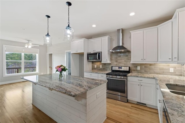 kitchen featuring appliances with stainless steel finishes, white cabinetry, wall chimney range hood, light wood-type flooring, and backsplash