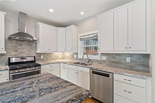 kitchen with a sink, white cabinets, appliances with stainless steel finishes, wall chimney range hood, and backsplash