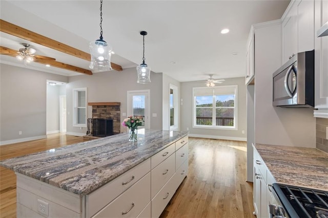 kitchen featuring a ceiling fan, open floor plan, white cabinetry, appliances with stainless steel finishes, and a fireplace