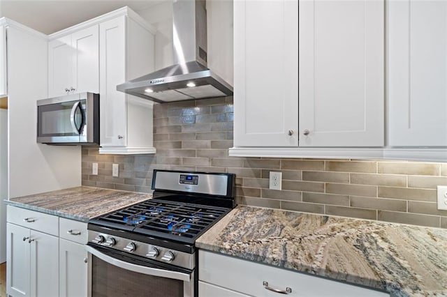 kitchen featuring light stone counters, stainless steel appliances, white cabinetry, wall chimney range hood, and tasteful backsplash