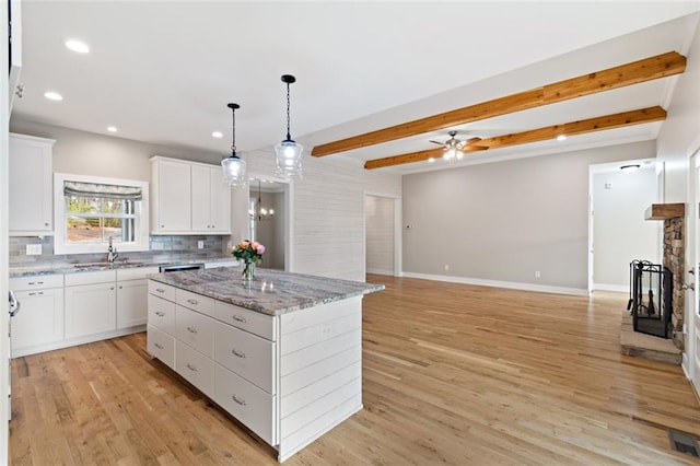 kitchen featuring a fireplace, decorative backsplash, beamed ceiling, light wood-type flooring, and a center island