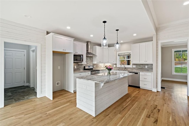 kitchen with a sink, wall chimney range hood, white cabinets, and stainless steel appliances