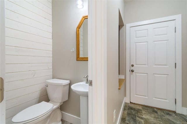 half bath with stone finish flooring, baseboards, and toilet