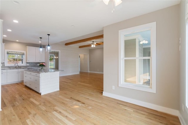 kitchen with a ceiling fan, open floor plan, a center island, white cabinetry, and light wood finished floors