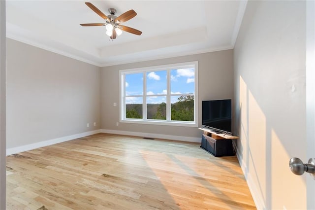 unfurnished living room featuring baseboards, ornamental molding, light wood-style flooring, a raised ceiling, and a ceiling fan