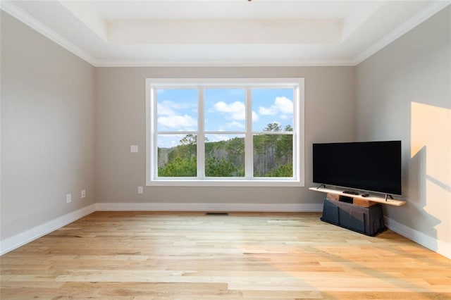 unfurnished living room with a raised ceiling, crown molding, baseboards, and light wood-type flooring