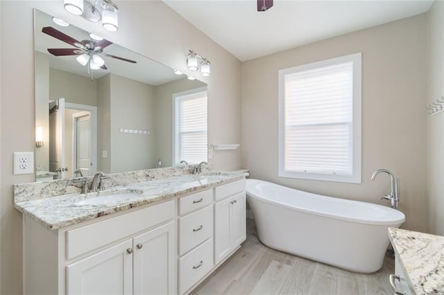 full bathroom with wood finished floors, double vanity, a freestanding tub, a ceiling fan, and a sink