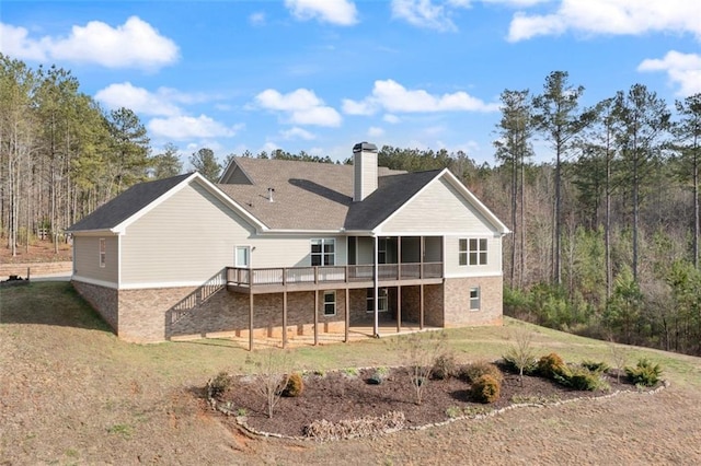 rear view of property featuring stairway, a forest view, a chimney, a deck, and a lawn