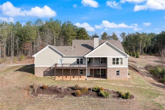 back of property with a deck, stairway, a yard, a wooded view, and a chimney