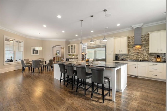 kitchen with arched walkways, gas stovetop, backsplash, wall chimney exhaust hood, and dark wood finished floors