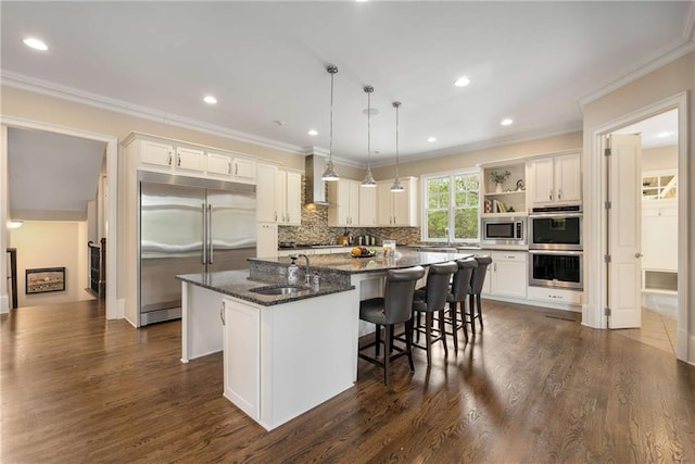 kitchen featuring open shelves, a spacious island, a sink, wall chimney range hood, and built in appliances