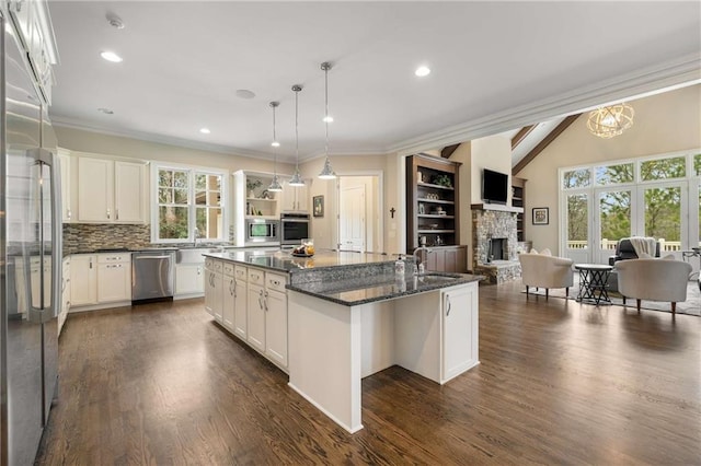 kitchen with built in appliances, lofted ceiling with beams, a stone fireplace, a kitchen island with sink, and a sink