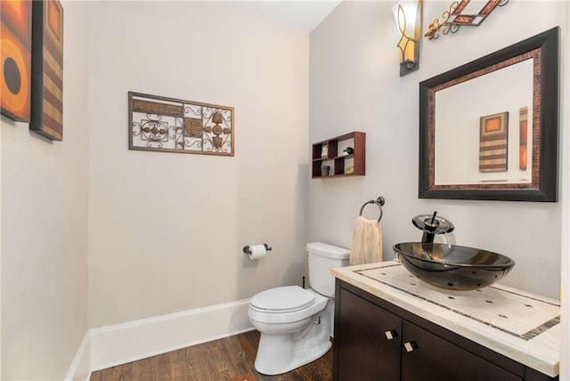 half bathroom with baseboards, vanity, toilet, and wood finished floors