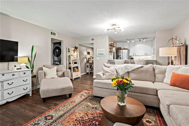 living room featuring dark hardwood / wood-style floors, stacked washer and clothes dryer, and a textured ceiling