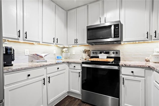 kitchen with stainless steel appliances, light stone countertops, white cabinets, and backsplash