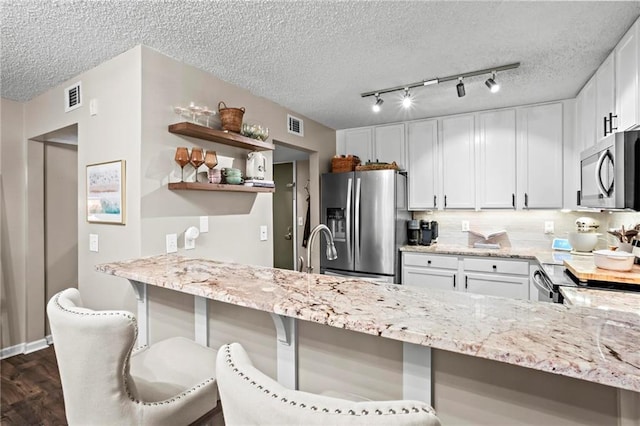 kitchen with white cabinetry, stainless steel appliances, a textured ceiling, and a kitchen bar