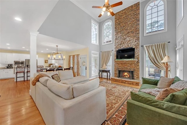 living room with light wood finished floors, a high ceiling, ornate columns, a fireplace, and ceiling fan with notable chandelier