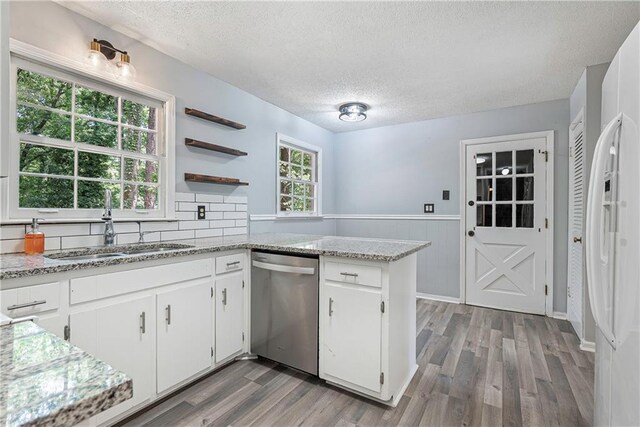 kitchen with hardwood / wood-style floors, white cabinets, dishwasher, kitchen peninsula, and a textured ceiling