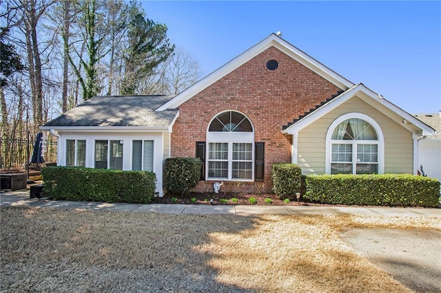 view of front of house with a shingled roof, a front yard, and brick siding