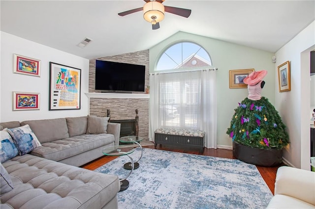 living room with lofted ceiling, visible vents, a ceiling fan, a stone fireplace, and wood finished floors