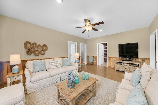 living area with tile patterned floors, a wainscoted wall, and a ceiling fan