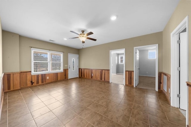 tiled spare room featuring wooden walls, wainscoting, visible vents, and a ceiling fan