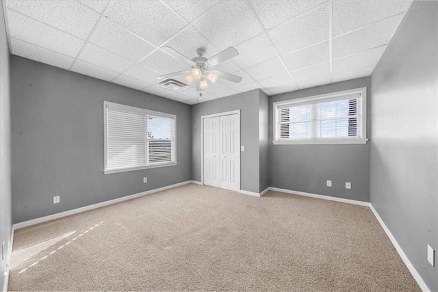 unfurnished bedroom featuring a drop ceiling, carpet floors, baseboards, and a closet