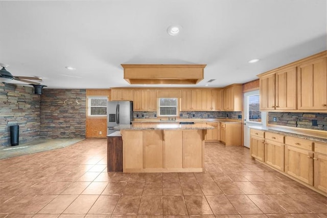 kitchen with light brown cabinetry, decorative backsplash, stainless steel fridge, and a center island