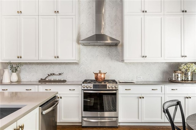 kitchen featuring tasteful backsplash, white cabinets, wall chimney exhaust hood, and appliances with stainless steel finishes