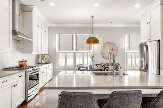 kitchen featuring pendant lighting, appliances with stainless steel finishes, an island with sink, white cabinets, and wall chimney exhaust hood