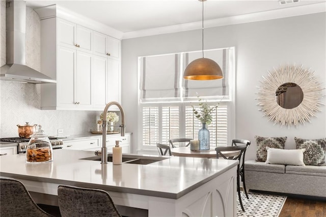 kitchen featuring sink, hanging light fixtures, white cabinets, decorative backsplash, and wall chimney exhaust hood