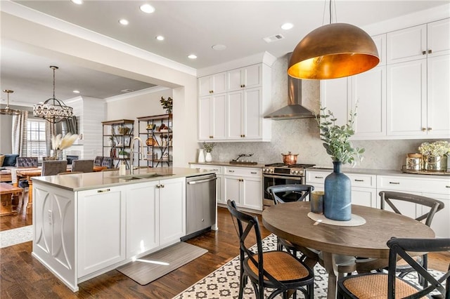 kitchen with wall chimney range hood, hanging light fixtures, an island with sink, and appliances with stainless steel finishes