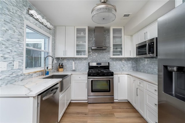 kitchen featuring wall chimney exhaust hood, sink, light stone counters, stainless steel appliances, and white cabinets