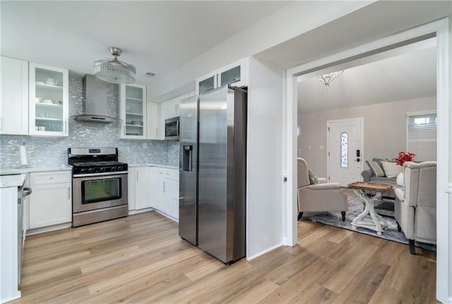 kitchen featuring appliances with stainless steel finishes, white cabinets, light hardwood / wood-style floors, and wall chimney exhaust hood