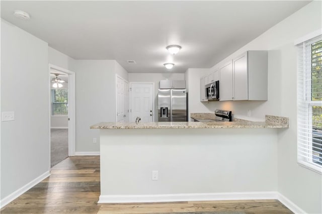 kitchen with ceiling fan, light stone counters, kitchen peninsula, wood-type flooring, and appliances with stainless steel finishes