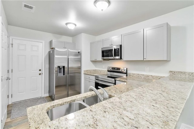 kitchen featuring sink, appliances with stainless steel finishes, light hardwood / wood-style floors, light stone counters, and kitchen peninsula