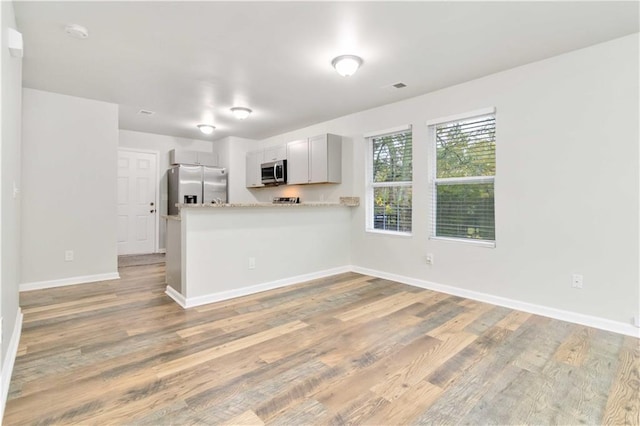 kitchen with kitchen peninsula, appliances with stainless steel finishes, light hardwood / wood-style floors, and white cabinetry