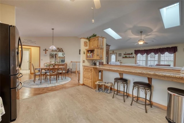 kitchen featuring vaulted ceiling with skylight, light countertops, a ceiling fan, pendant lighting, and freestanding refrigerator