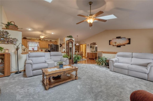 carpeted living area with vaulted ceiling with skylight and a ceiling fan