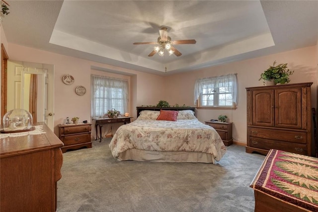 bedroom with a ceiling fan, a tray ceiling, and light colored carpet