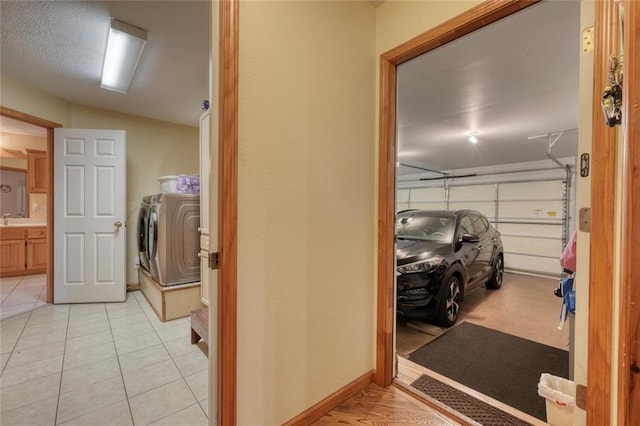 interior space with washing machine and dryer, laundry area, light tile patterned floors, baseboards, and a garage